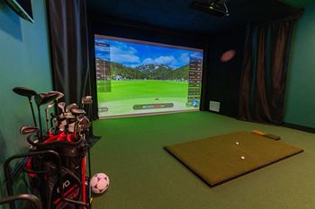A golf simulator room with a screen, golf clubs, and a ball.